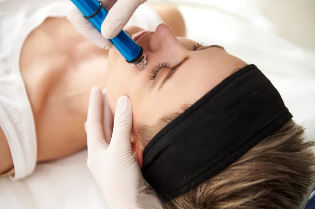 Hydrafacial Deluxe behandeling waarbij een huidtherapeut het gezicht reinigt met vacuümtechnologie voor diepgaande huidverbetering en een zichtbaar frissere huid