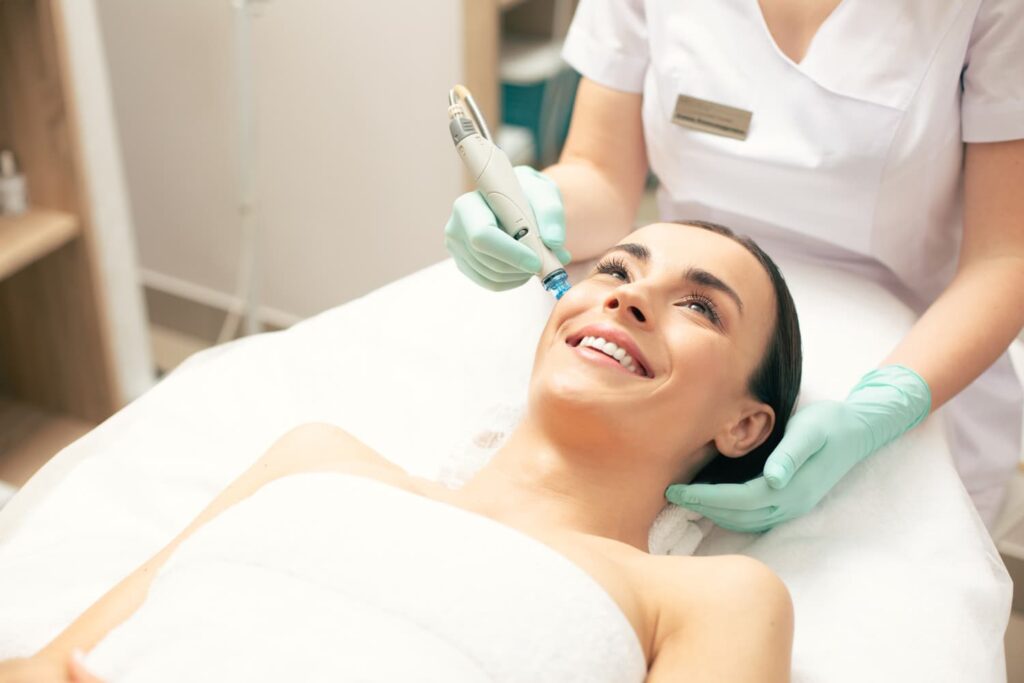 Lachende vrouw ondergaat hydrafacial behandeling op neus Vrouw geniet van hydrafacial behandeling — professionele huidverzorging voor cliënten uit Den Haag en omgeving